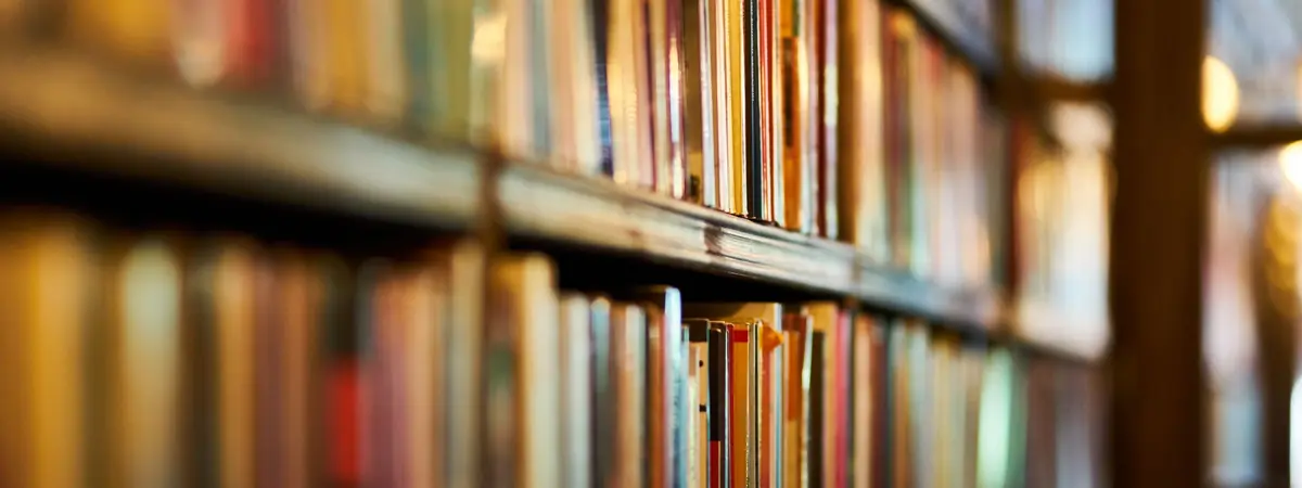 Rows of books with colorful spines filling long wooden library shelves, softly out of focus