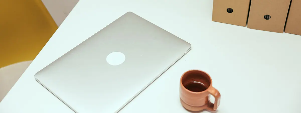 A tidy white office desk with a closed laptop, a clay mug and cardboard file holders