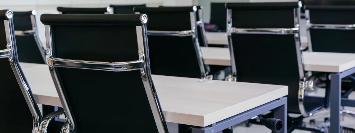 Black leather office chairs pulled up to light wood tables in an empty meeting room