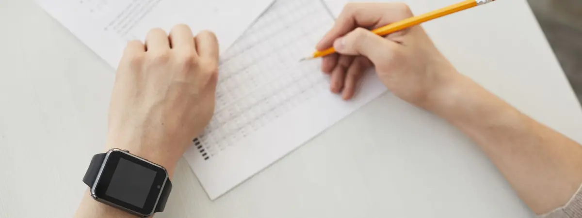 Seen from above, a test taker fills in a bubble answer sheet with a yellow pencil