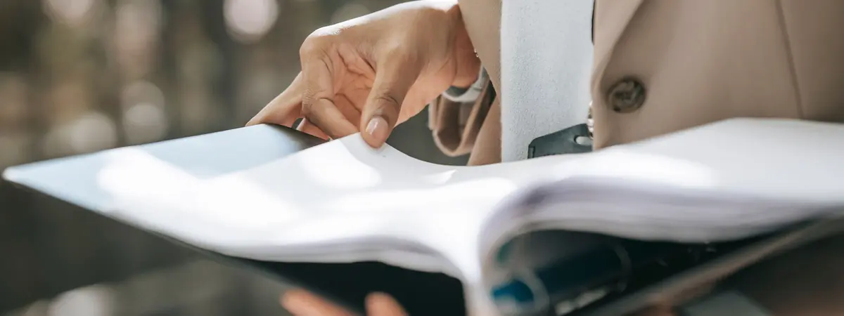 A professional in a tan blazer pages through a thick black ring binder of documents