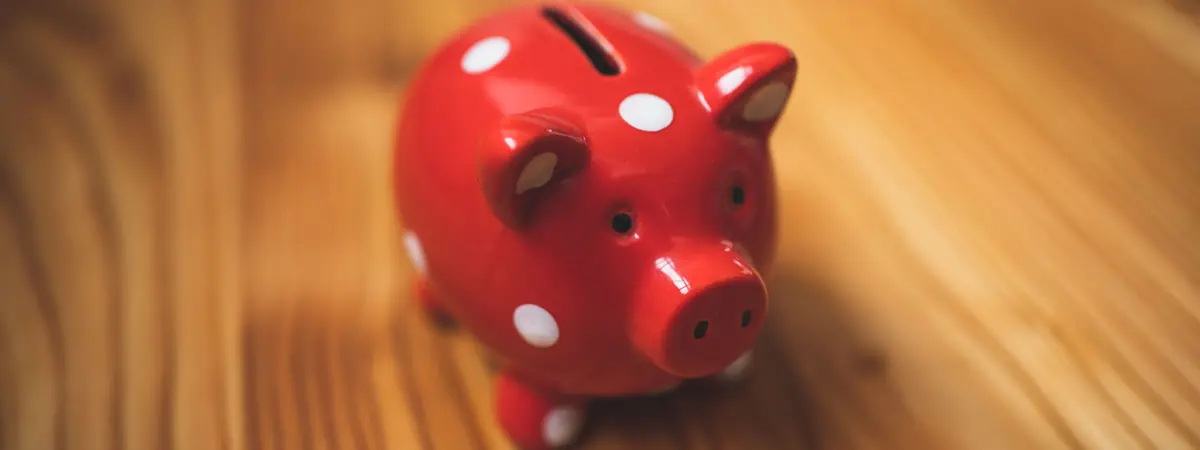 A small red piggy bank with white polka dots standing on a light wooden tabletop
