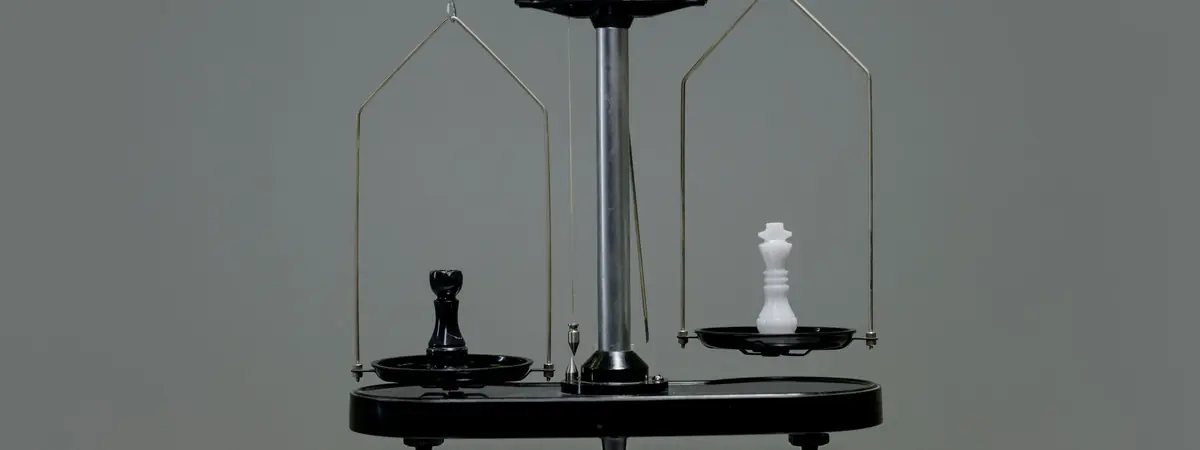 A balance scale tipping toward a black chess rook, with a white king on the other pan