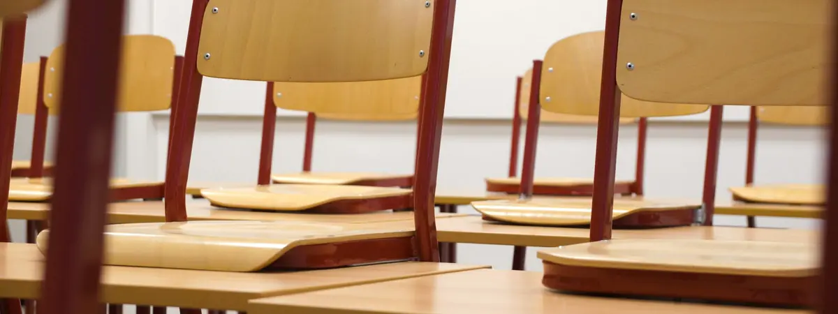Wooden classroom chairs turned upside down on rows of desks in an empty classroom