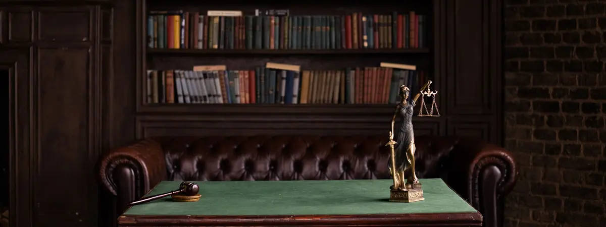 A law library desk with a gavel and a Lady Justice figure before shelves of books